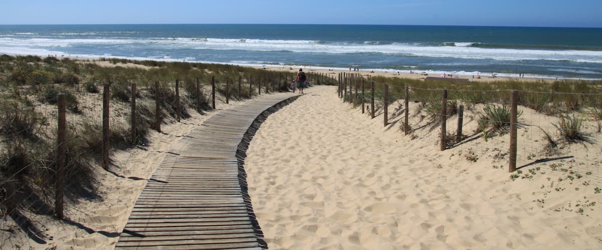 A sandy beach with a wooden boardwalk and a fence.