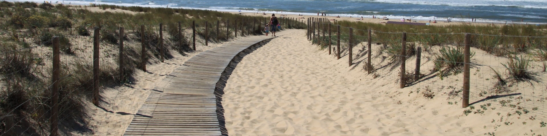 A sandy beach with a wooden boardwalk and a fence.