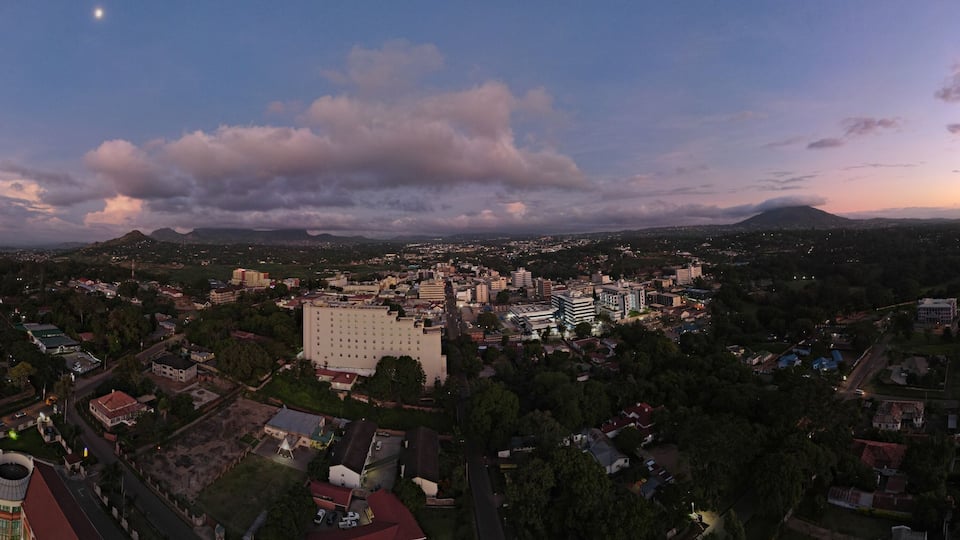 A cityscape at dusk with a prominent building in the center, surrounded by residential areas and a mountain in the background.