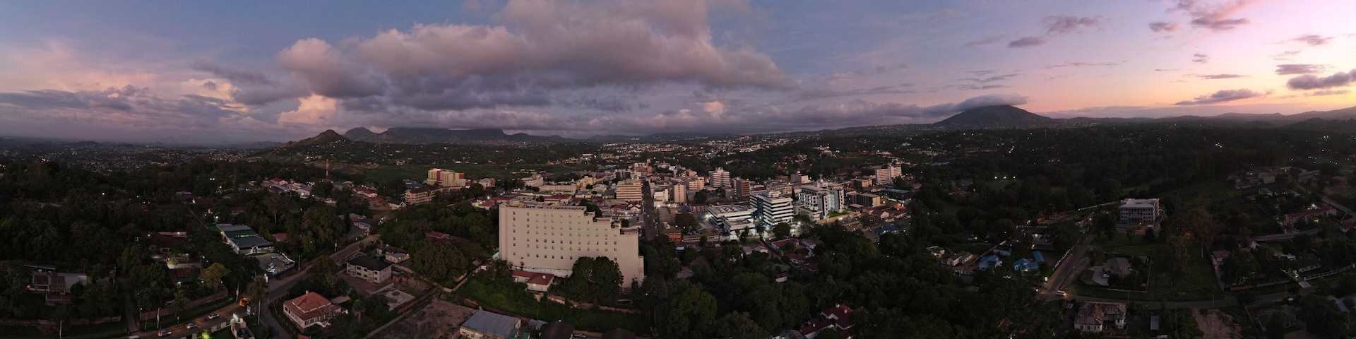 A cityscape at dusk with a prominent building in the center, surrounded by residential areas and a mountain in the background.