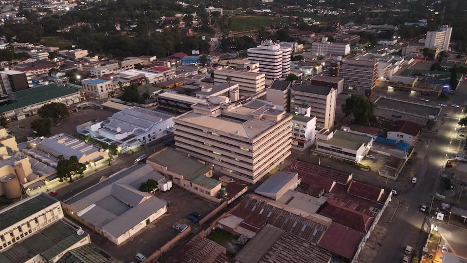 An aerial view of a cityscape with a prominent multi-story building, a mix of commercial and residential buildings, and a river in the background.