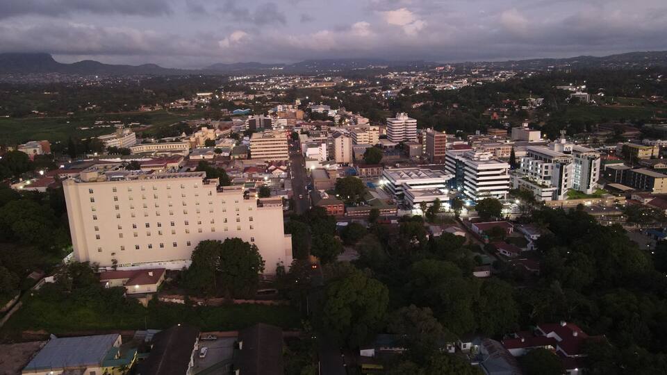 A cityscape at dusk with a large hotel, several commercial buildings, and a distant mountain range.