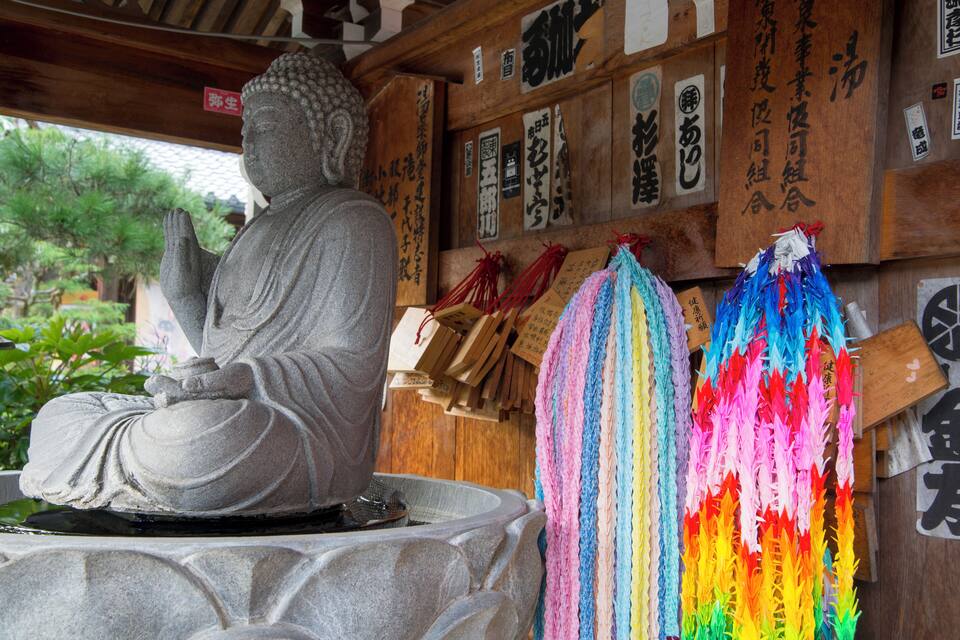 Une statue de Bouddha en pierre, dans un temple aux murs en bois, ornée de calligraphies japonaises.