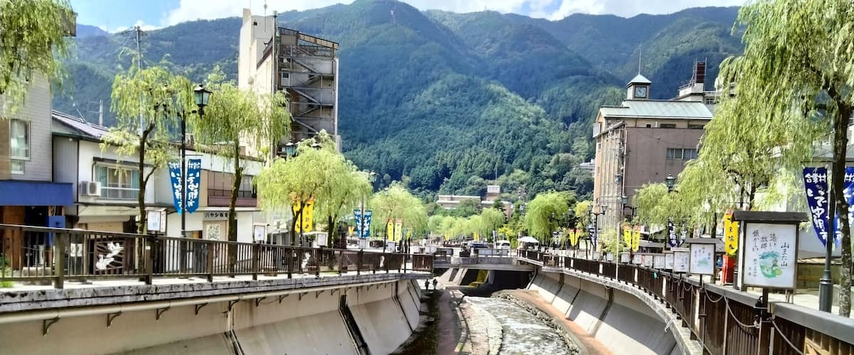 A river flowing through a town with a bridge, buildings, and mountains in the background.