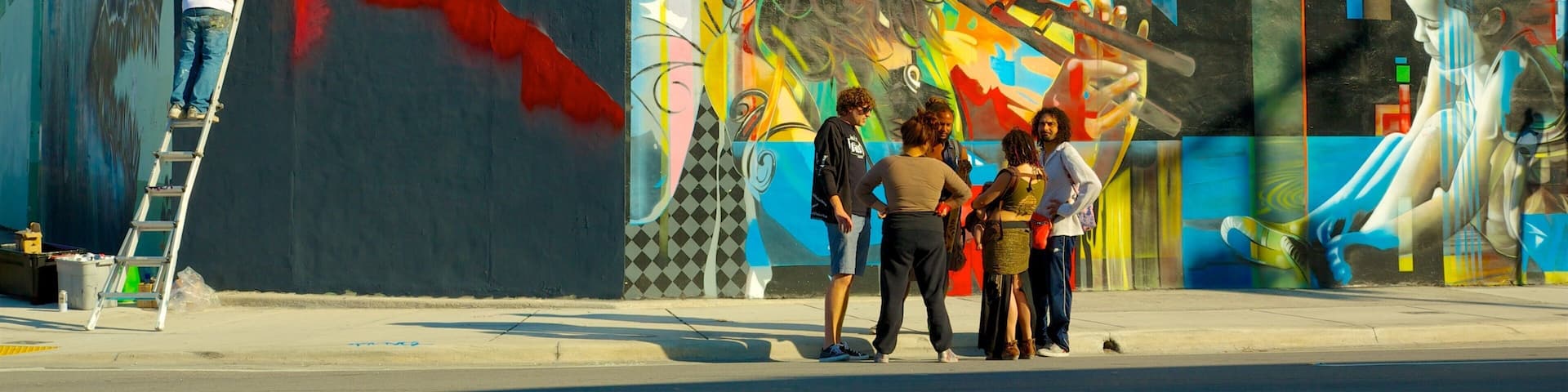 A mural on a building with a ladder and people observing it.