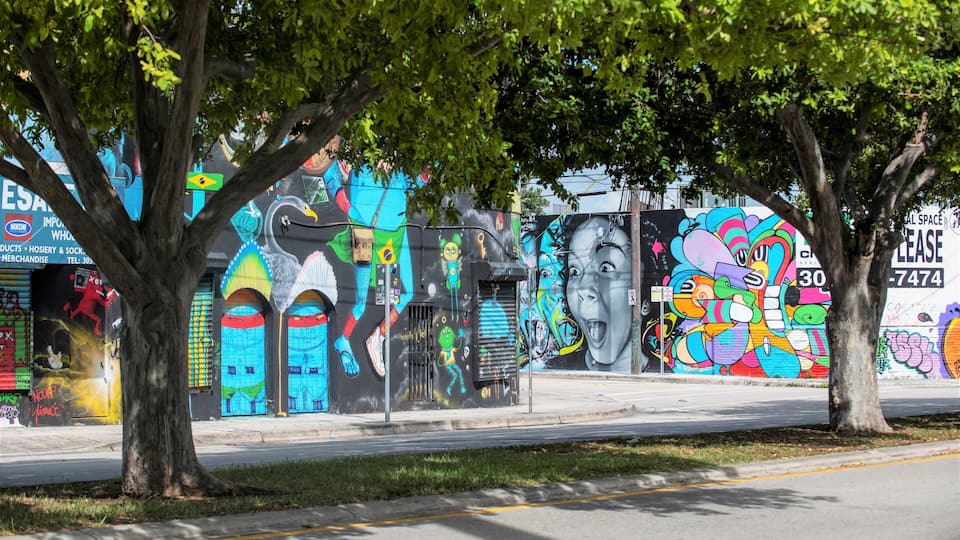 A colorful mural on a building, trees, and a sidewalk.