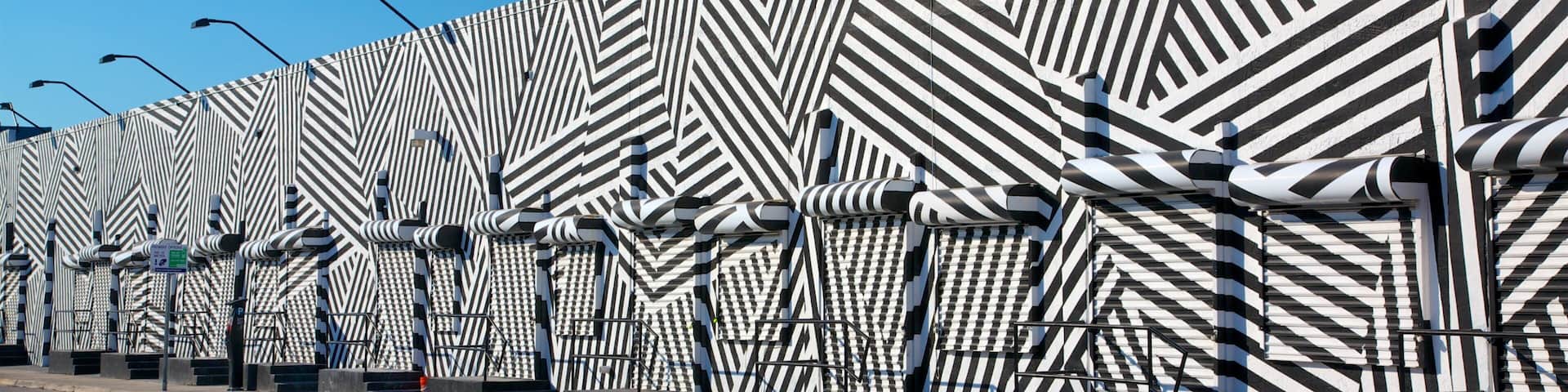 A patterned wall with geometric designs and street lamps along a road.