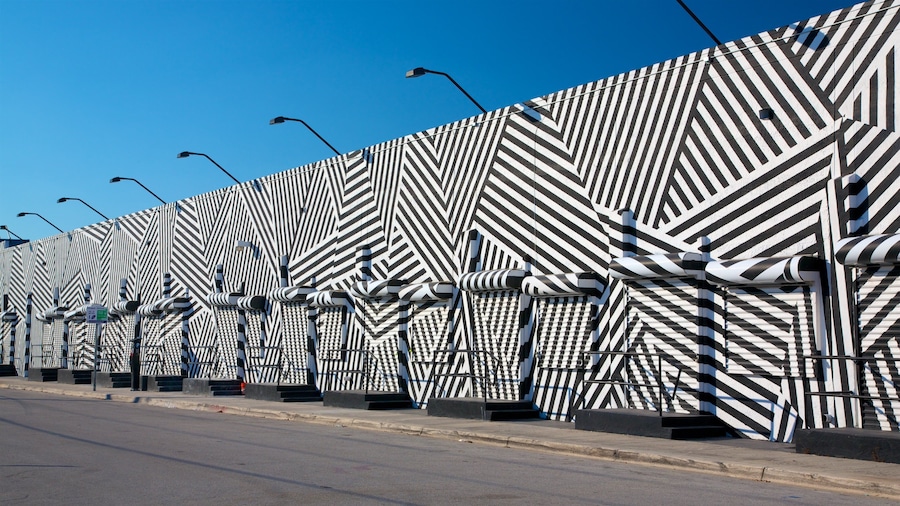 Un mur orné de motifs géométriques et des lampadaires le long d’une route.