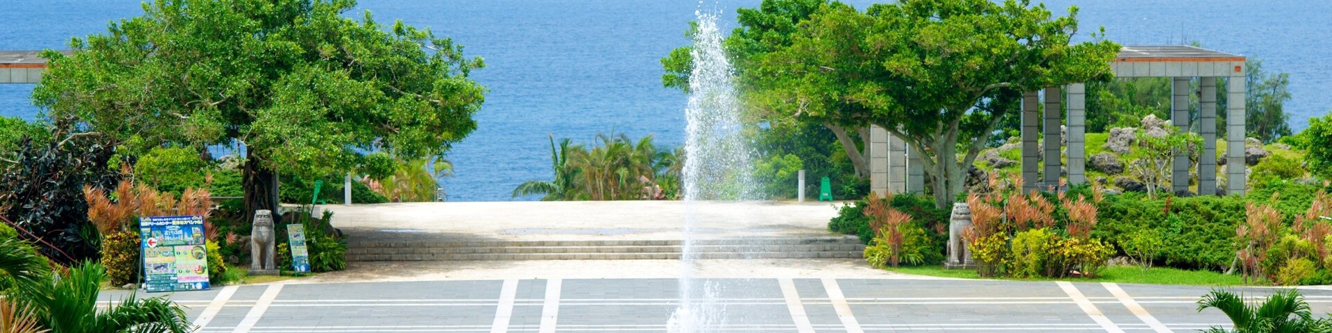A fountain in a plaza with a view of the ocean and a mountain in the distance.