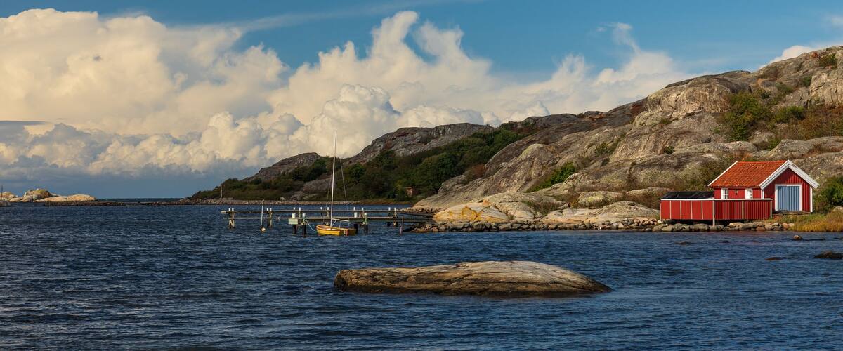 A coastal scene with a rocky shoreline, a red building, and a wooden dock extending into the water.