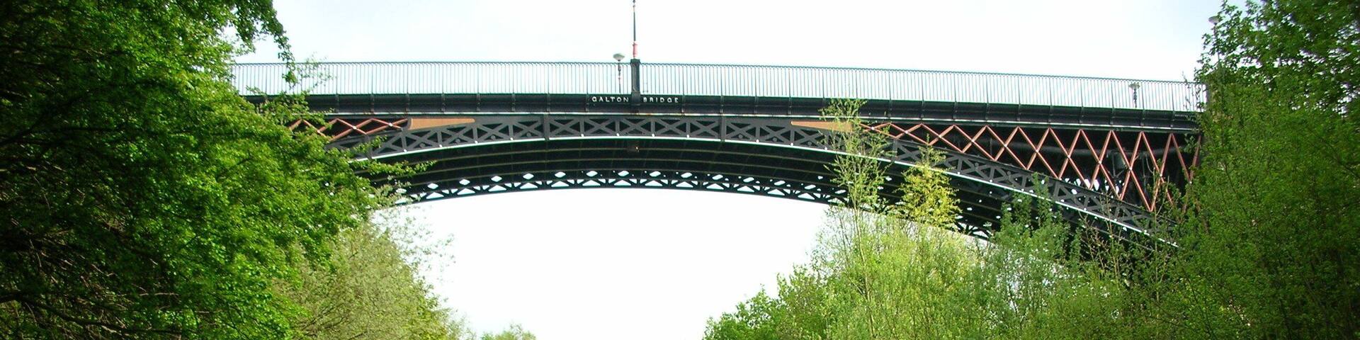 A river under a bridge with dense greenery on both sides.