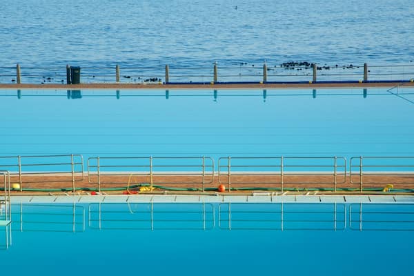 Piscina com deck de madeira e grades de metal.