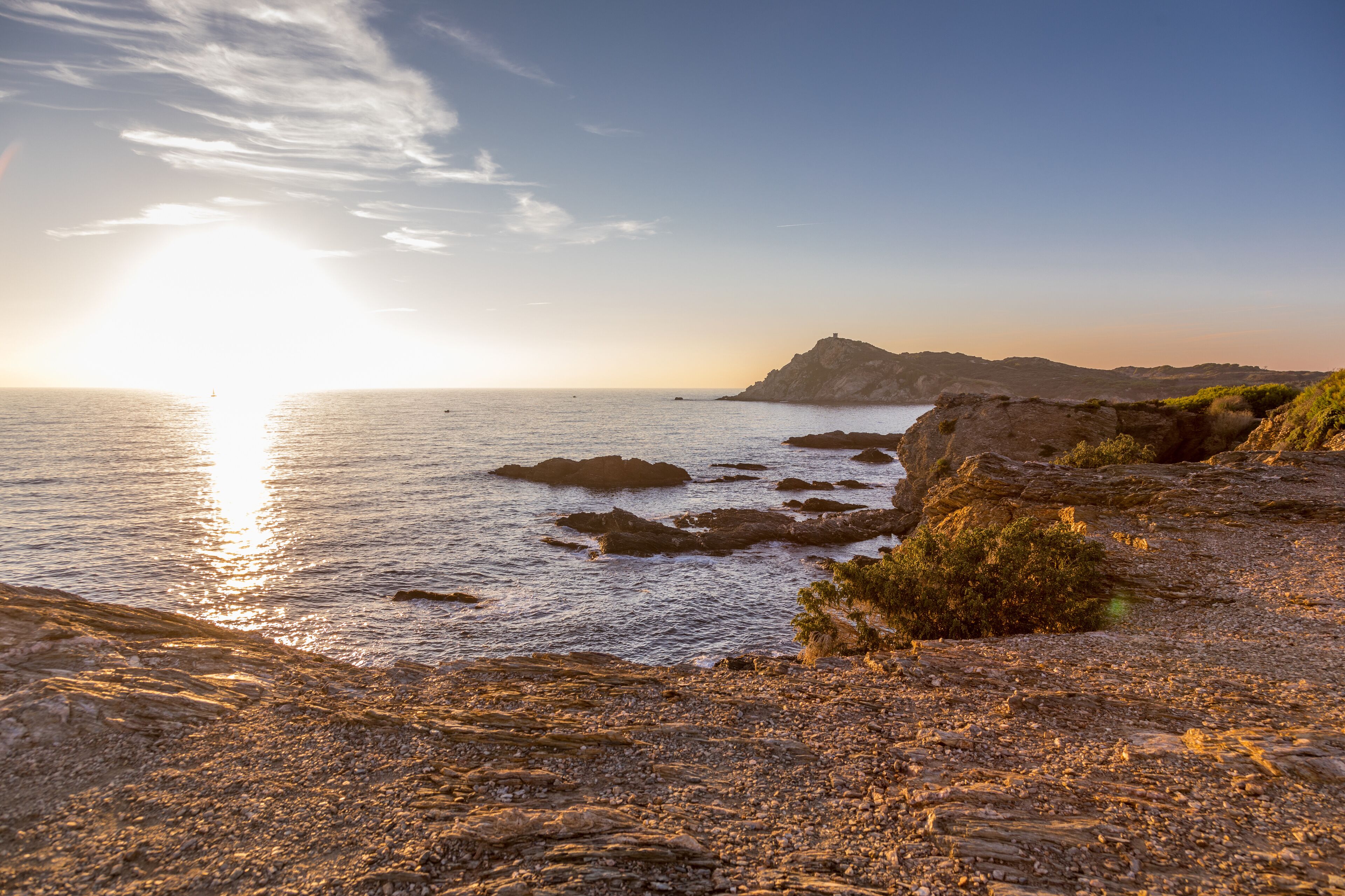 A rocky coastline with a lighthouse in the distance during sunset.