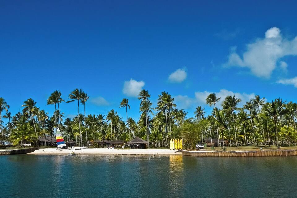 Een strand met palmbomen, een hut met rieten dak en een zeilboot.