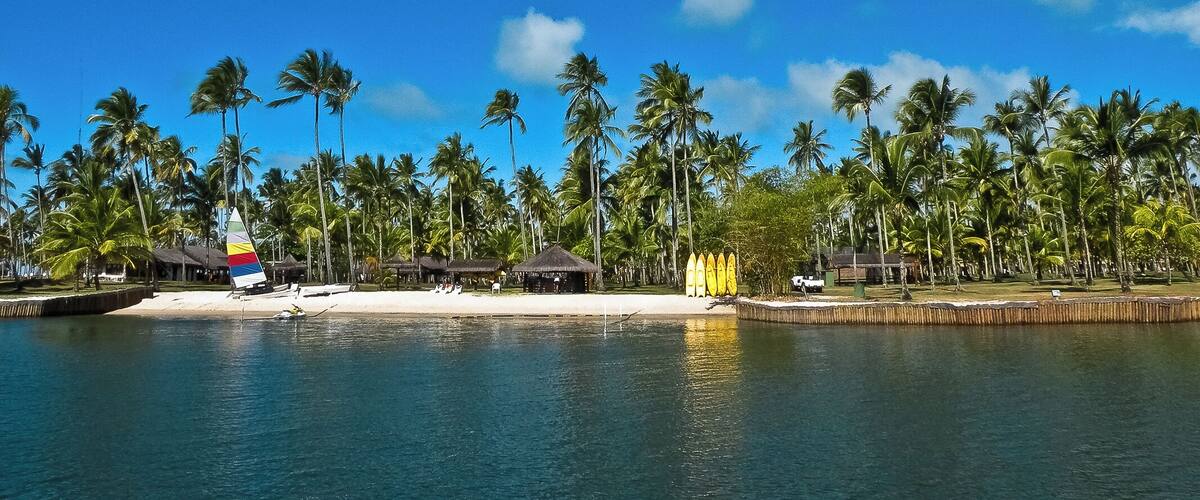 A beach with palm trees, a thatched-roof hut, and a sailboat.