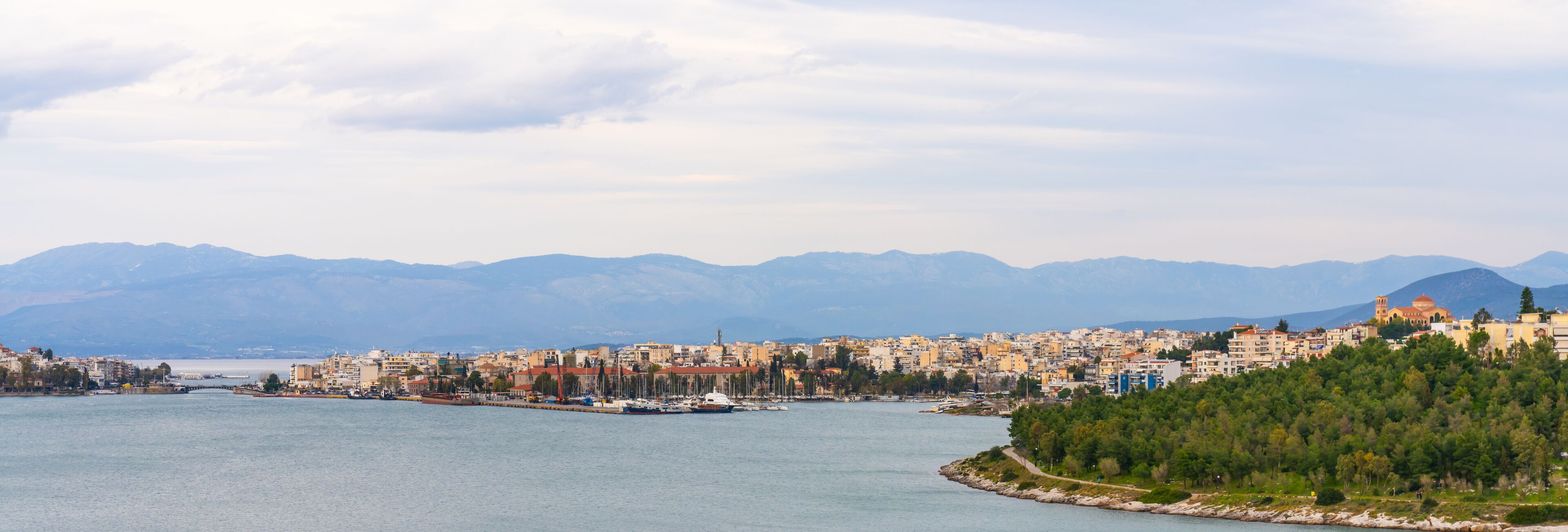 A coastal city with a harbor, mountains in the background, and a prominent church on a hill.