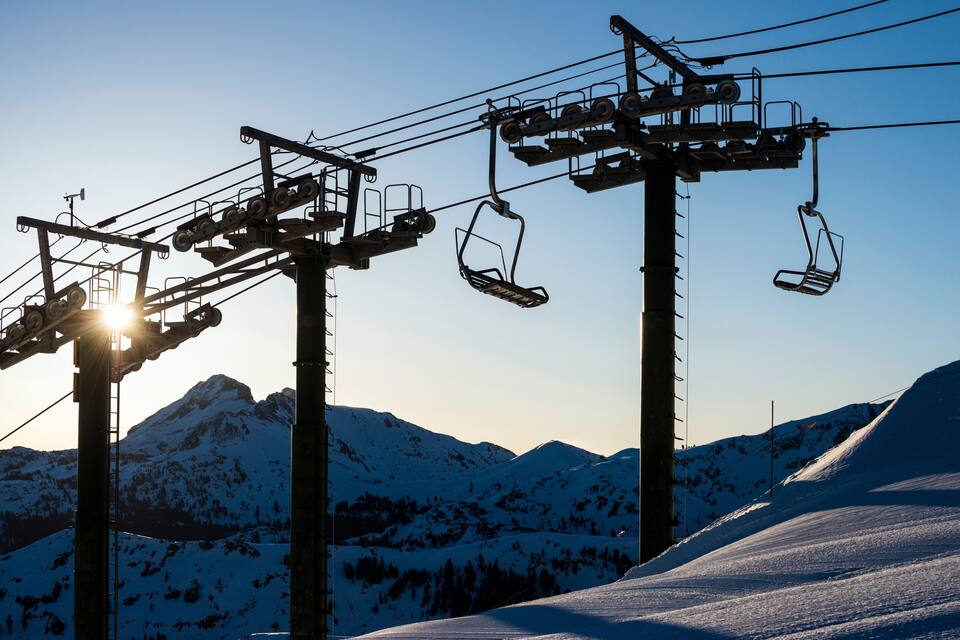Eine Seilbahn mit Kabeln vor verschneiter Berglandschaft bei Sonnenuntergang.