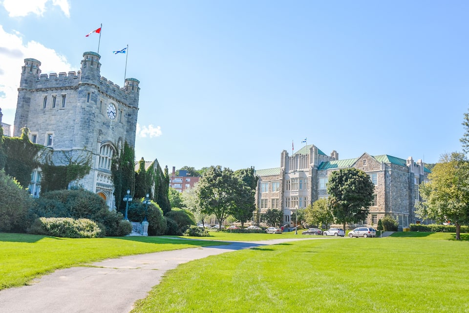 A castle with a clock tower, surrounded by lush green lawns and trees.