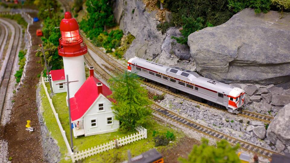 A model train with a red and white locomotive passing a white church with a red roof and a red lighthouse.