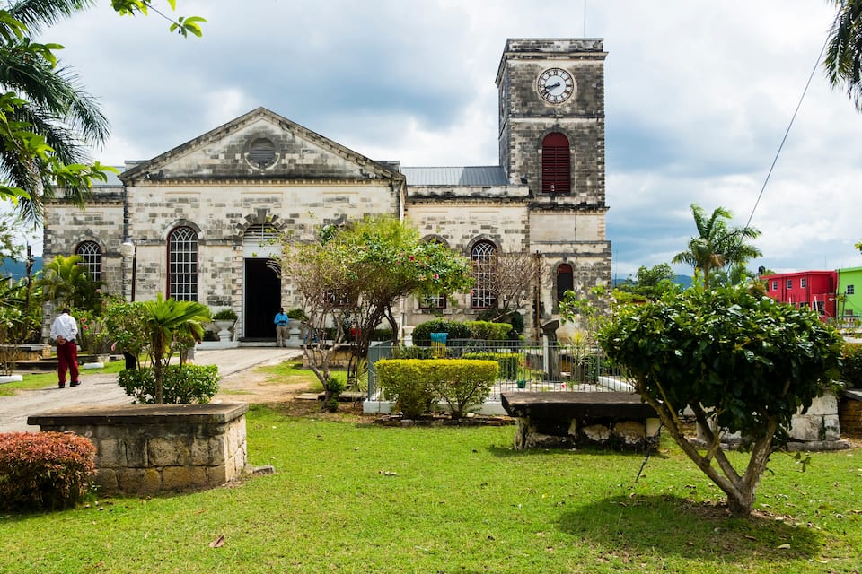 A historic stone building with a clock tower, surrounded by lush greenery and a well-maintained lawn.