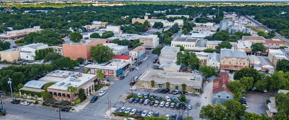 An aerial view of a town with a mix of historic and modern buildings, a central street, and surrounding greenery.