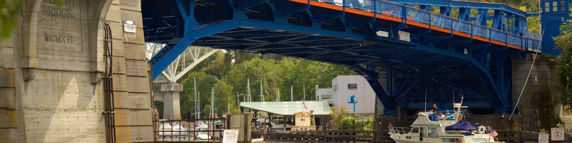 Uma ponte azul sobre um rio, com barcos e um cais.