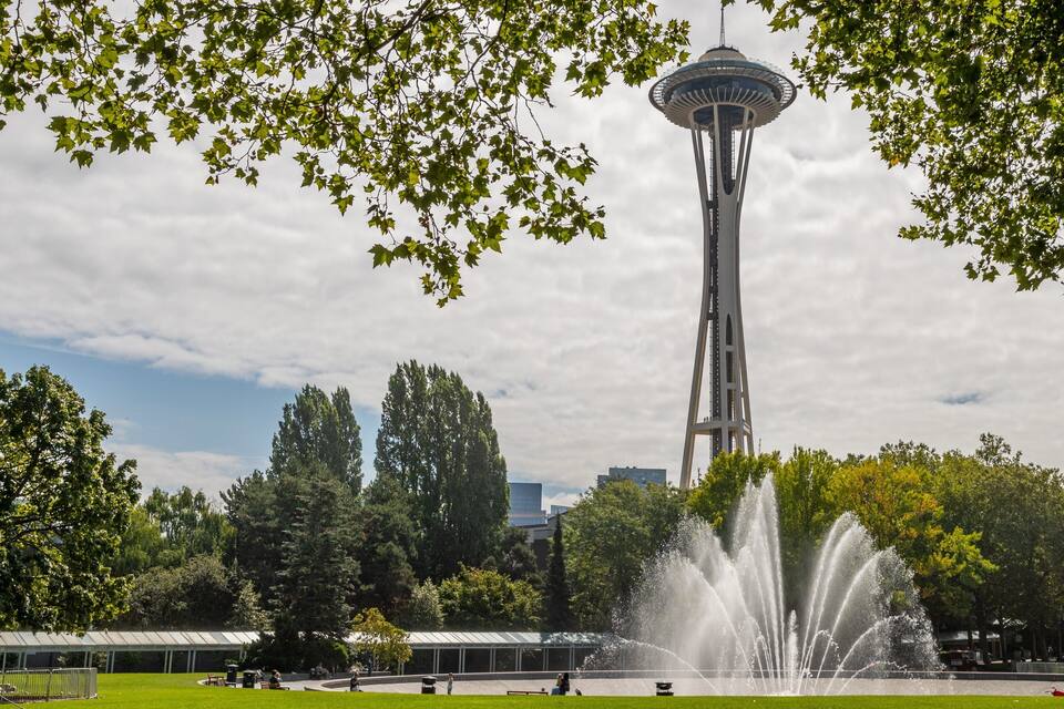 A park with a fountain, trees, and a tower.