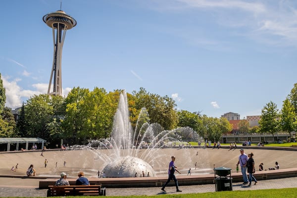 Ein Park mit einem Wasserspeier, Menschen, einem hohen Turm und Bäumen.