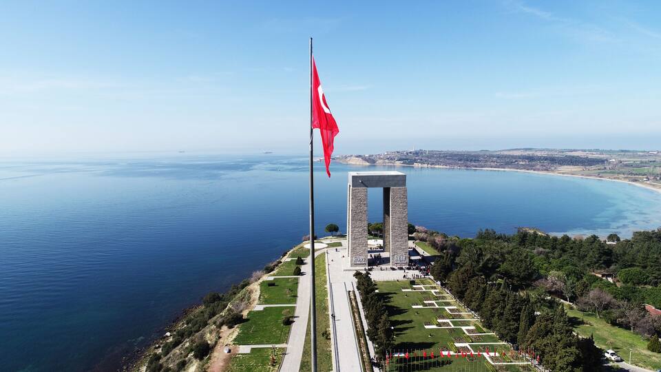 A coastal cityscape with a prominent monument and a flagpole with a red flag.