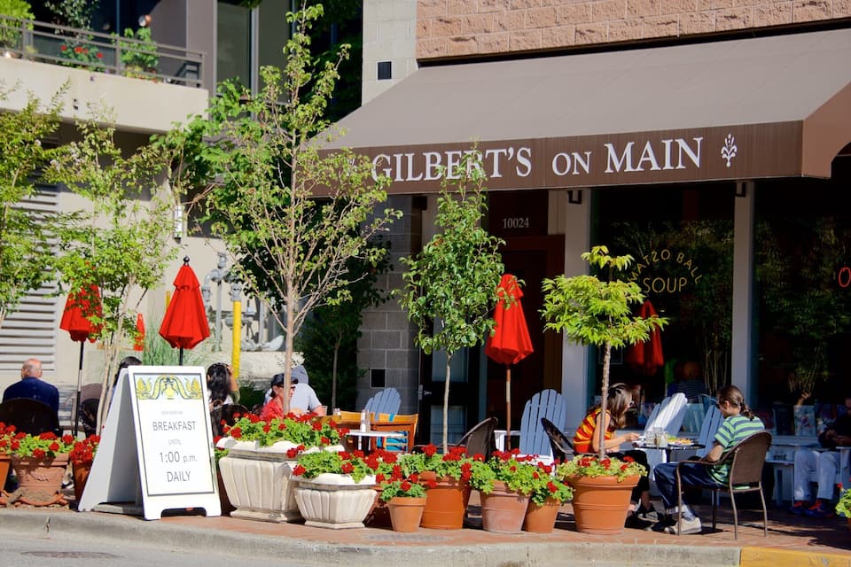 Un restaurante llamado 'Gilbert's on Main' con terraza y sombrillas rojas.