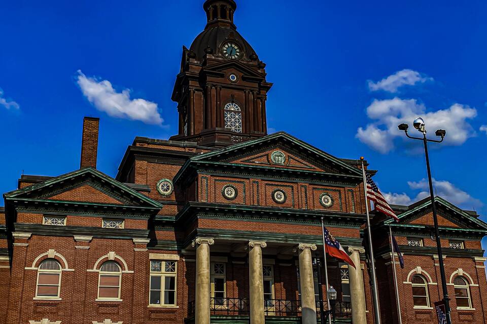 Um grande edifício de tijolos com uma torre de relógio imponente, colunas e a bandeira americana.