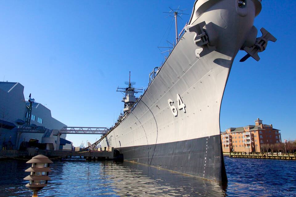 A large ship docked at a port with a bridge and buildings in the background.