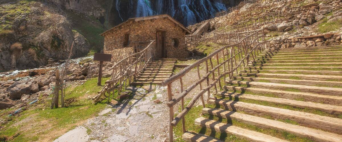 A stone building with wooden stairs leading to a waterfall.