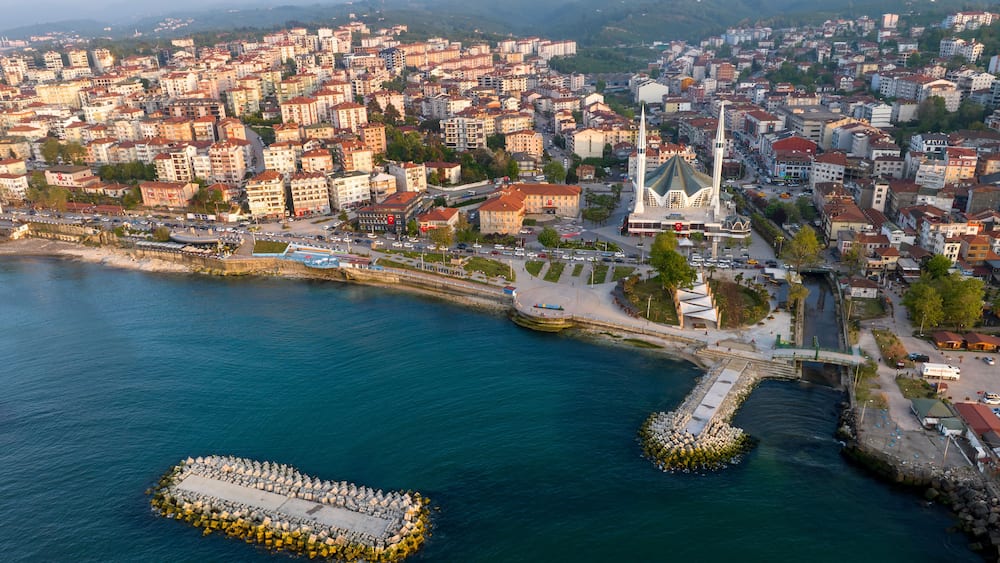 Vue aĂ©rienne dâune ville cĂŽtiĂšre avec des bĂątiments urbains denses, une Ă©glise blanche imposante et une structure circulaire en pierre situĂ©e dans lâeau.