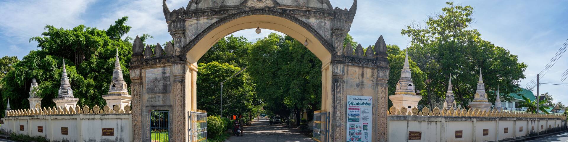 A historic gate with intricate carvings, flanked by traditional structures and lush greenery.