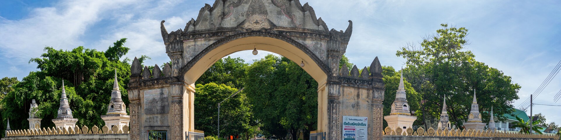 Una puerta histórica con intrincados grabados, flanqueada por construcciones tradicionales y abundante vegetación.