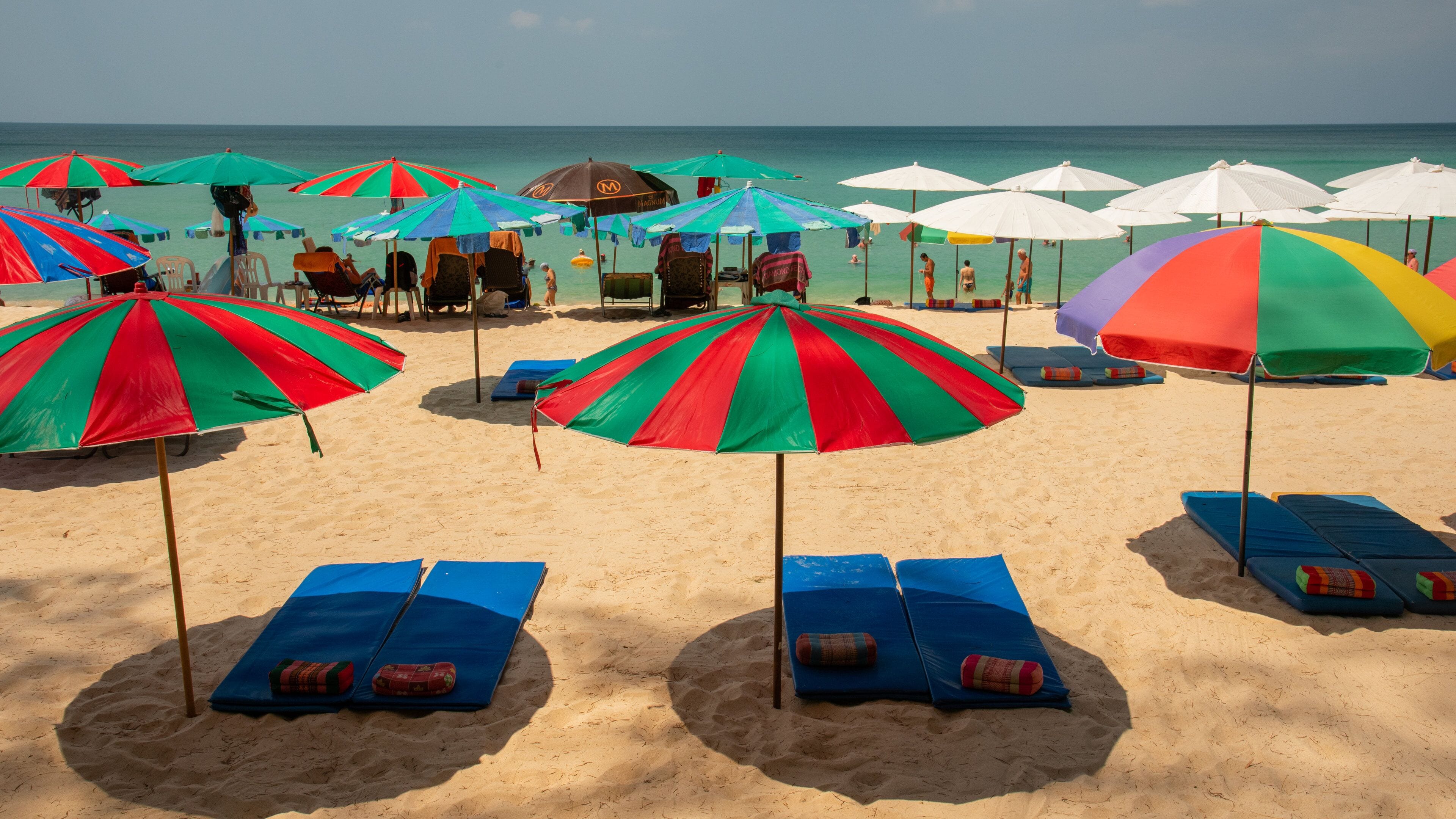 A beach with colorful umbrellas and blue lounge chairs.