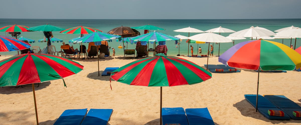 A beach with colorful umbrellas and blue lounge chairs.