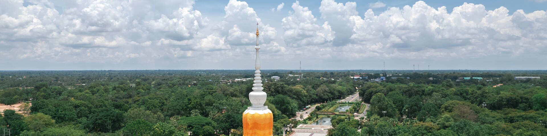 Un gran stupa blanco y amarillo rodeado de exuberante vegetación y un cielo azul despejado.