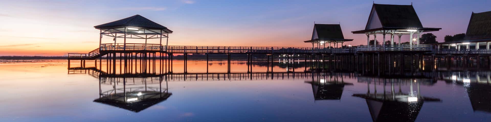 A tranquil waterfront with overwater bungalows and a wooden pier reflecting the sunset.