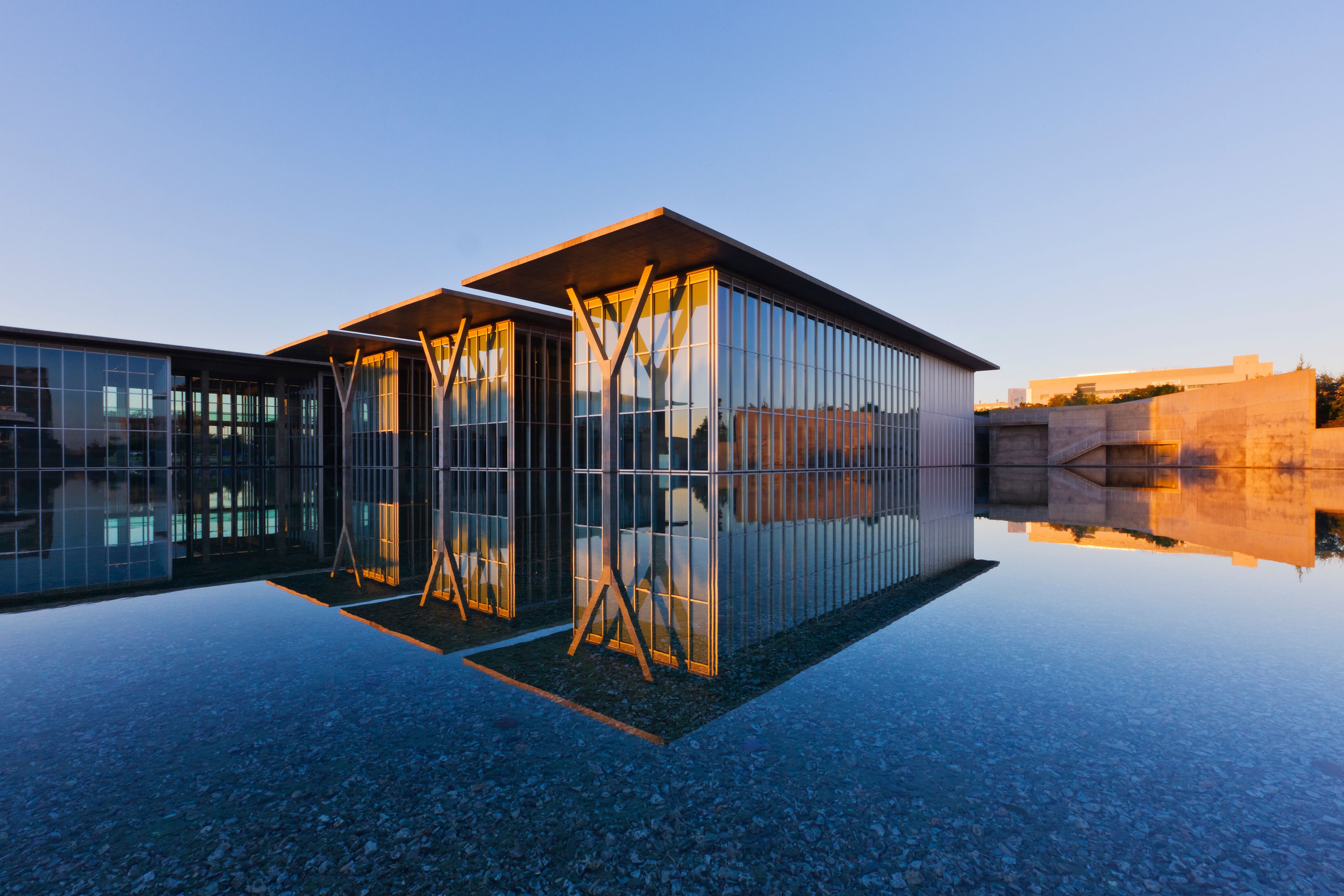 A modern glass building with a reflective surface, surrounded by a clear blue sky.