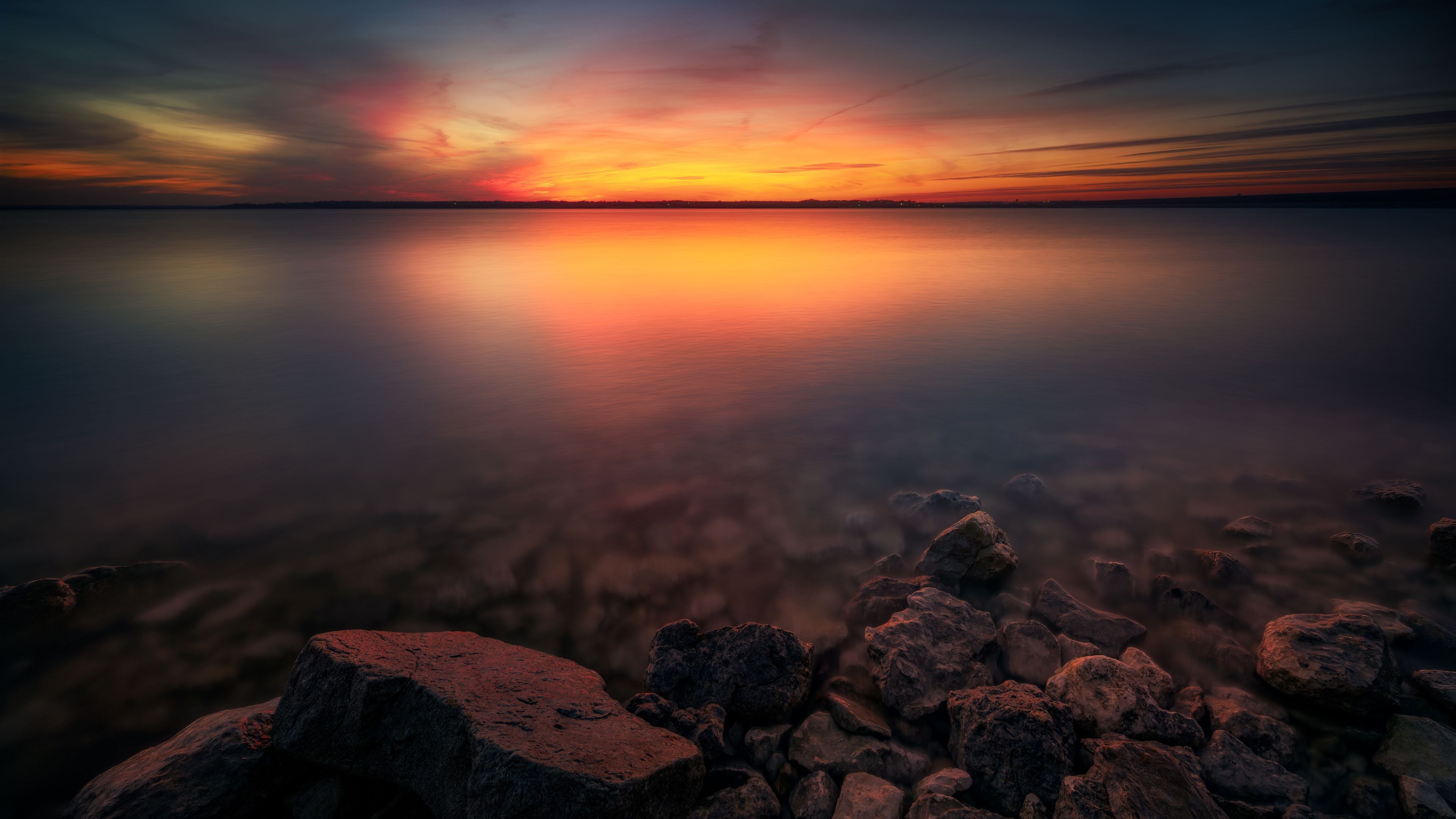A sunset over a calm body of water with a rocky shoreline in the foreground.
