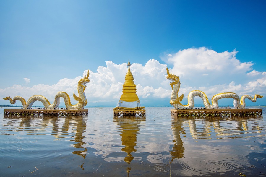 Een gouden stoepa omgeven door draak sculpturen op een spiegelglad wateroppervlak.