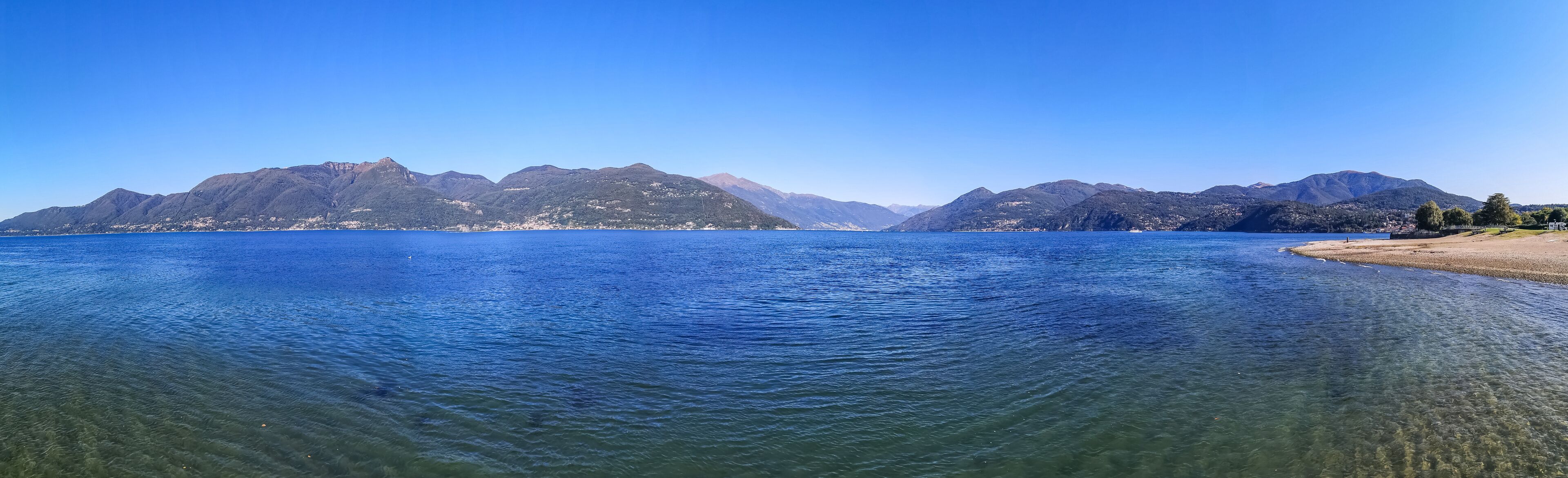 A calm lake with clear water, surrounded by mountains and a sandy beach.