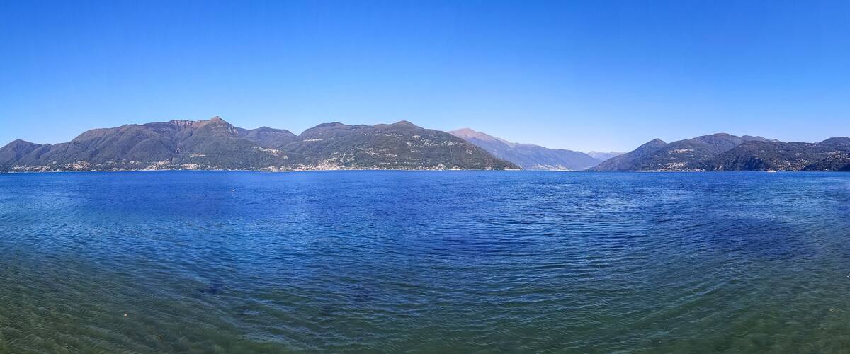 A calm lake with clear water, surrounded by mountains and a sandy beach.
