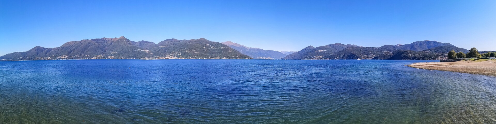 A calm lake with clear water, surrounded by mountains and a sandy beach.