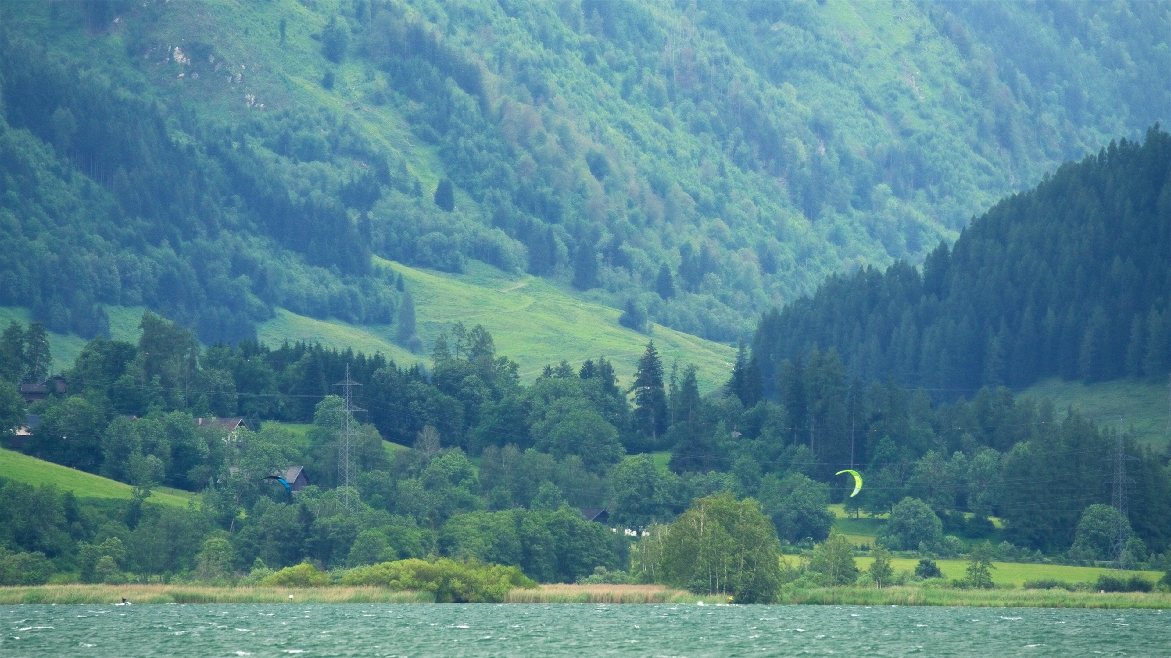 A lake surrounded by lush green hills and a forested mountain range.