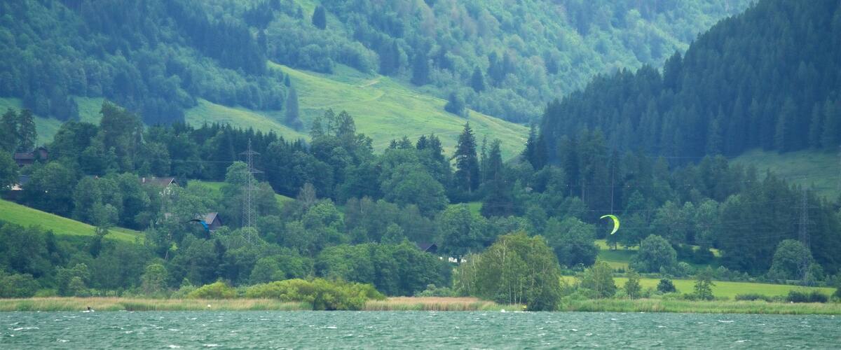 A lake surrounded by lush green hills and a forested mountain range.