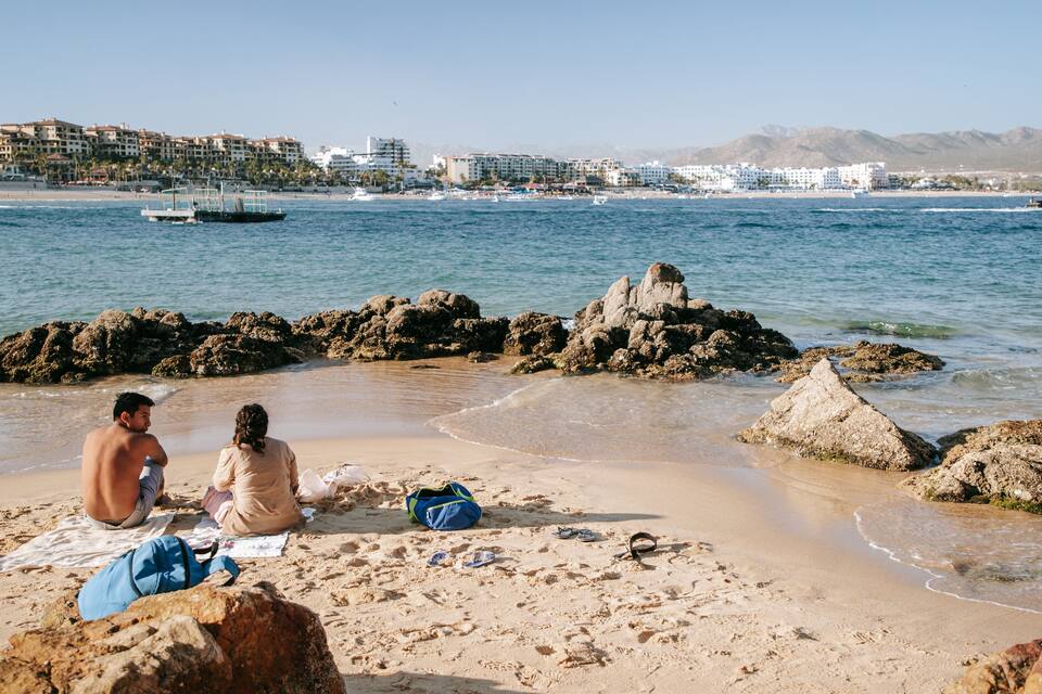 A beach with rocky formations and a distant cityscape.