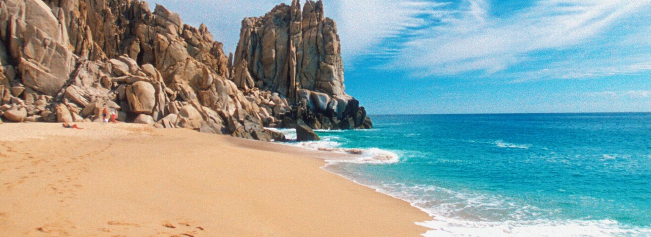 Una playa arenosa con un promontorio rocoso y cielo azul despejado.